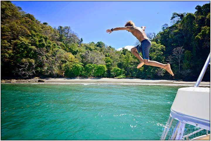 Guy jumping off boat into the ocean near a beach