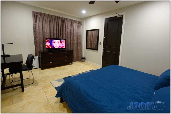 King size bed with blue cover, abstract blue carpet, TV on dresser, black desk and chair