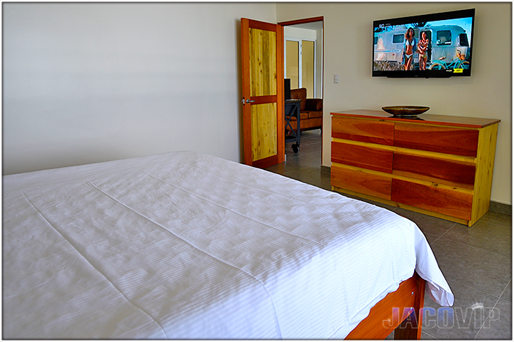 Flatscreen TV mounted on wall above wood dresser in bedroom