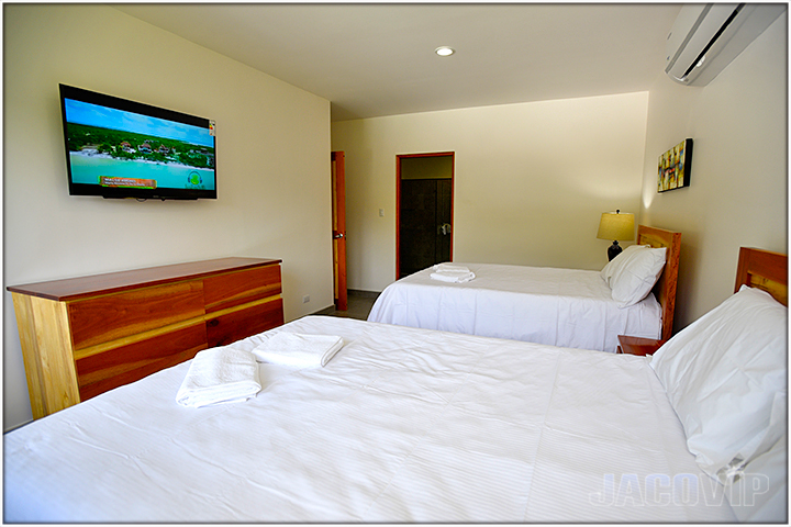 2 queen size beds and tv mounted to wall in bedroom