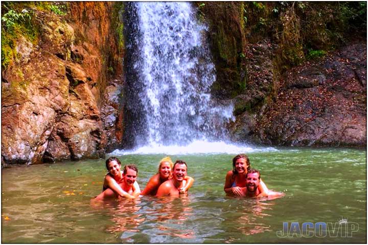 People swimming in front of waterfall