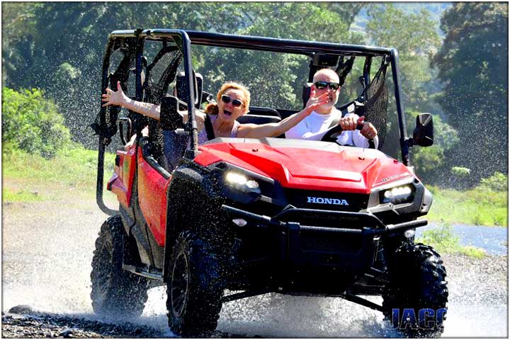 Couple driving Honda side by side vehicle across river in Costa Rica