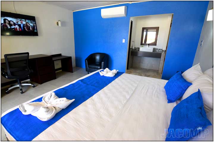 King bedroom with 2 black sofa chairs and large TV