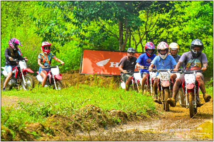 Group of people racing mini dirt bikes on muddy track
