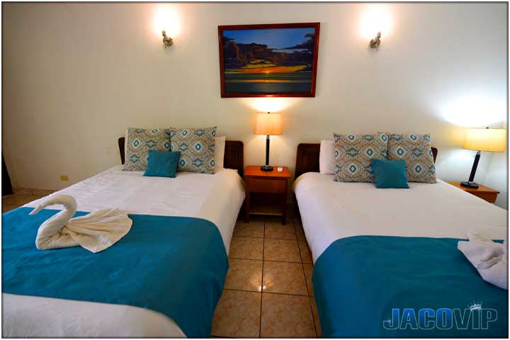 Straight on view of 2 queen size beds with teal color runners and accent pillows