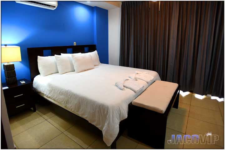 Blue wall behind king bed and lamp is on
