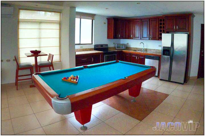 Pool table with balls inside triangle and view of secondary kitchen area used as bar