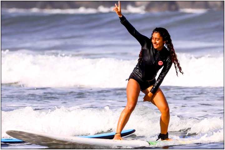 Girl standing up on surf board for the first time during lesson