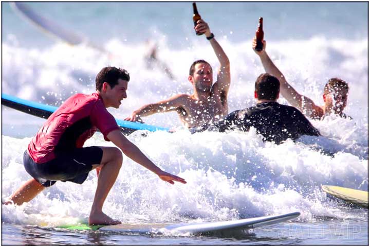 Guys drinking beer in the ocean during surf lessons