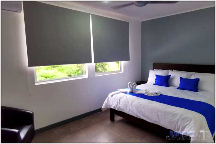 king size bed with white sheets, blue runner, grey wall and black chair