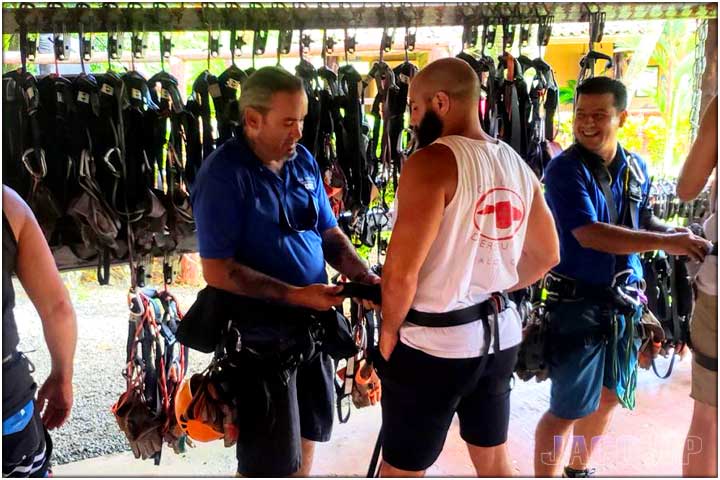 Guide at zipline canopy tour helping guest put on harness